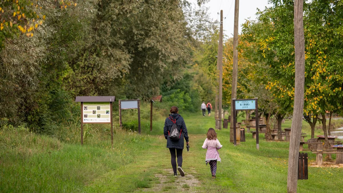 A parent and child walking on a path in a scenic nature reserve in Croatia, surrounded by lush greenery.