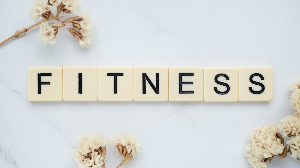 Close-up of scrabble tiles spelling 'FITNESS' on a marble surface with white flowers.